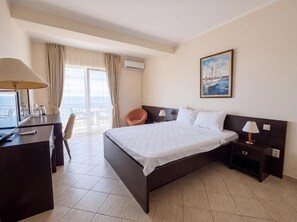 A hotel room with a bed, a desk, a chair, a nightstand, and a painting on the wall. - Casa Viktoria (Sveti Stefan)