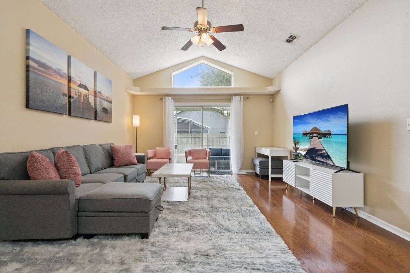 A living room with a gray sectional sofa, a coffee table, a TV, and artwork on the walls.
