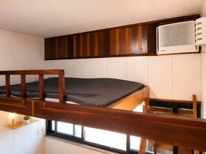Ein kleines Zimmer mit Etagenbett, kleinem Fenster und Wandklimaanlage.