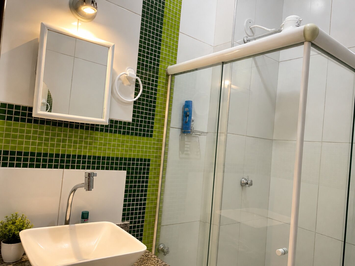 Une salle de bain avec un lavabo blanc, un miroir, une douche en verre et des murs recouverts de carreaux verts.