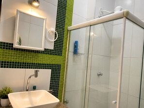 A bathroom with a white sink, a mirror, a glass shower enclosure, and green-tiled walls. - Vrbo Property (Rio de Janeiro)