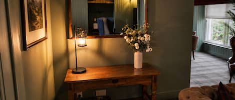 Een kamer met een ruiterig tapijt, een houten console tafel met een bloemenvaas, een ingelijste foto aan de muur en een bank.