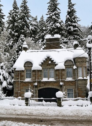 A stone building with multiple windows and a central entrance, surrounded by snow-covered trees. - Fairytale Scots Baronial Coach House in Ballater, near Balmoral Castle (Ballater)