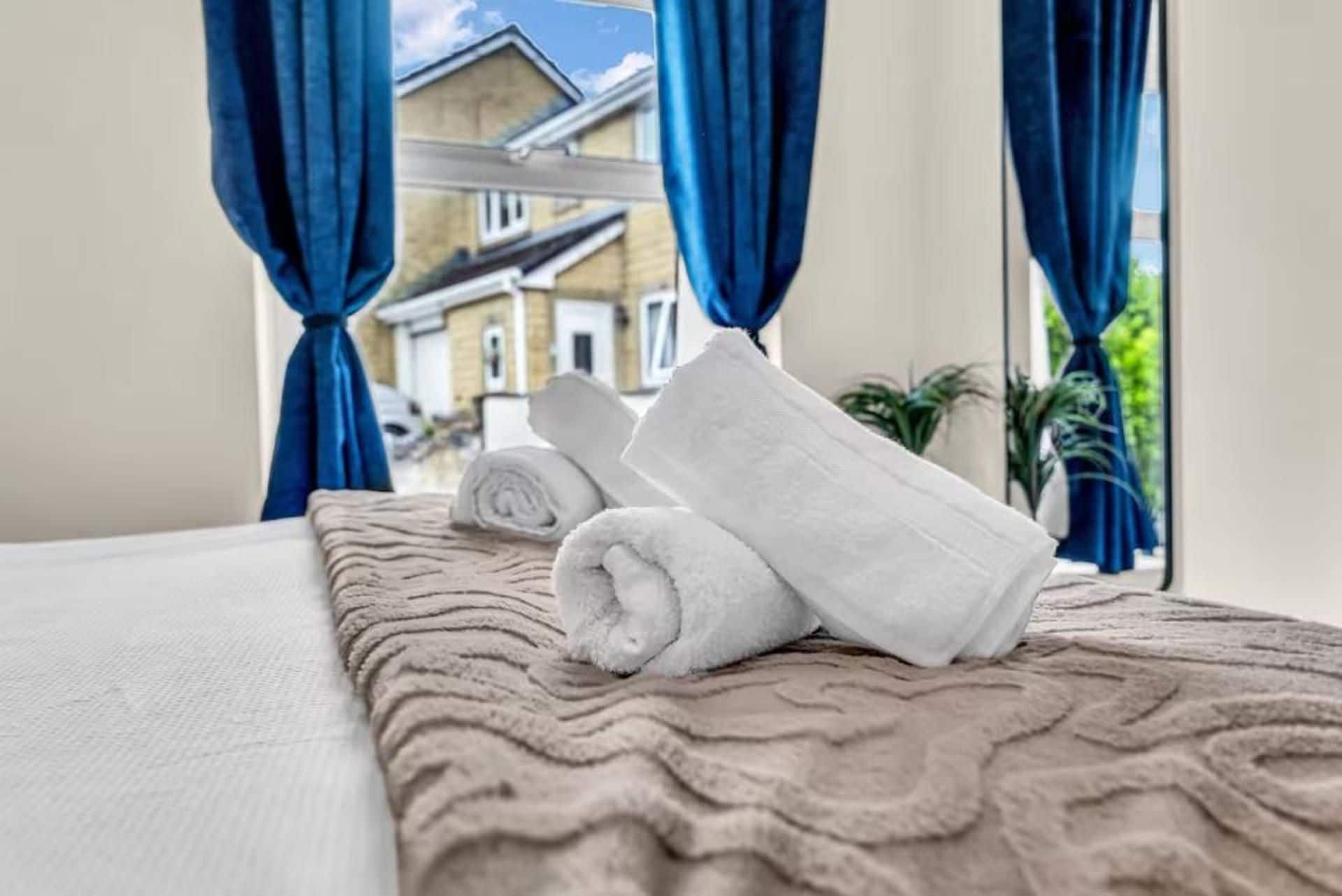 A bed with a beige textured bedspread and rolled white towels.