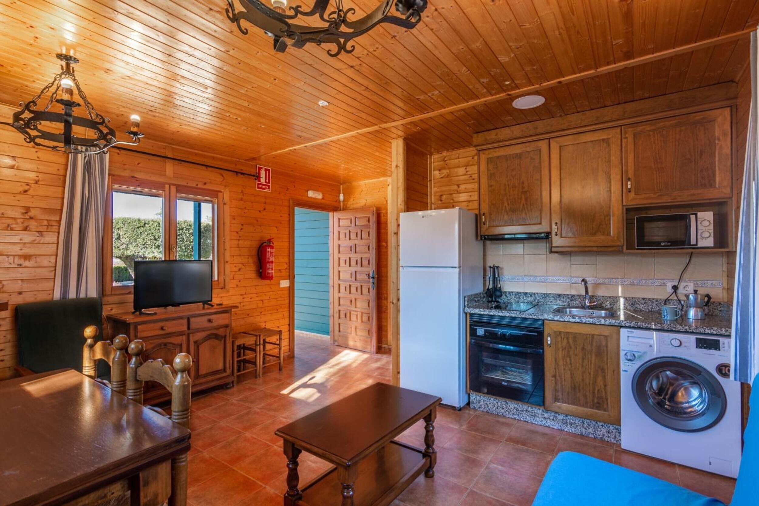 Un interior de madera con zona de comedor, cocina y televisor.