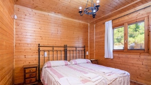 Ein Schlafzimmer mit Holzvertäfelung, einem Bett, einem Nachttisch, einer Kommode, einem Fenster mit Vorhängen und einer Kristallleuchtre.
