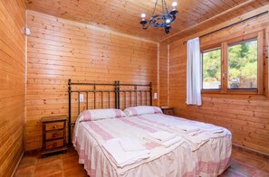 A wooden-paneled bedroom with a bed, a nightstand, a dresser, a window with curtains, and a chandelier. - Apartment 'El Estrecho' with Mountain View, Wi-Fi and Air Conditioning (Las Canales)