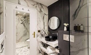 Une salle de bain avec un mur en marbre, un lavabo noir, un miroir et un porte-serviettes.