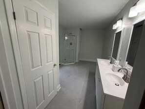 A bathroom with a double sink, a glass shower enclosure, and a white door.