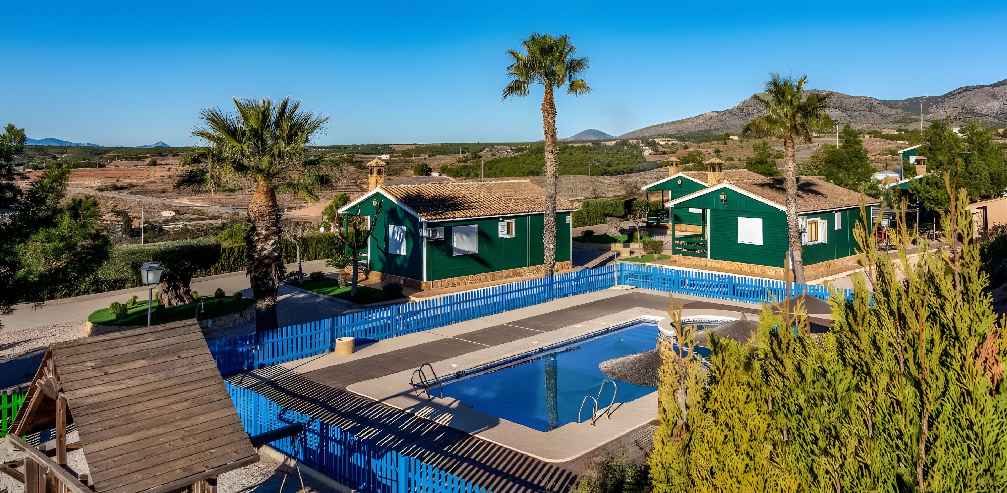 Una zona residencial con piscina, casas verdes y palmeras.