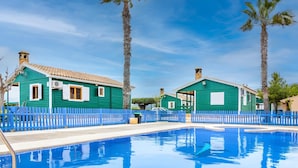 A swimming pool area with two green buildings, each with a window and a door, surrounded by a blue fence.