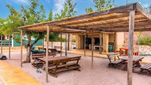 An outdoor patio area with wooden benches and tables, a covered seating area, and a stone wall in the background.