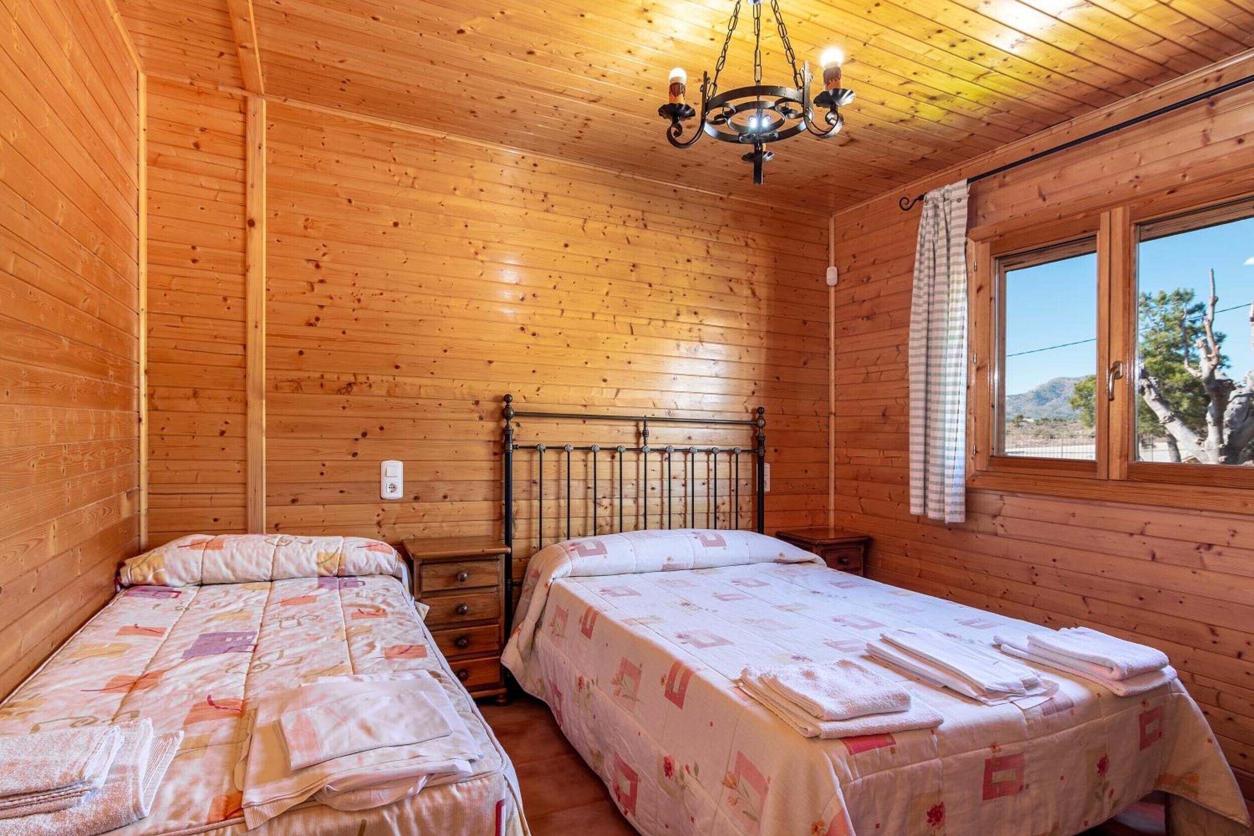 A room with two beds, wooden walls, a window, and a chandelier.