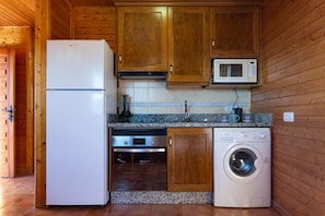 Cocina compacta con muebles de madera, refrigerador blanco, microondas, horno empotrado y lavadora de carga frontal.