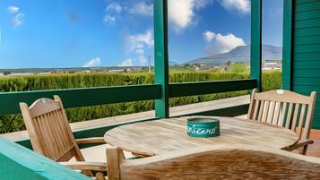 A wooden table with a green can on it, surrounded by wooden chairs, set on a balcony with a view of a green field and a mountain in the distance.