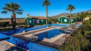 A pool area with a blue fence, green buildings, and palm trees.