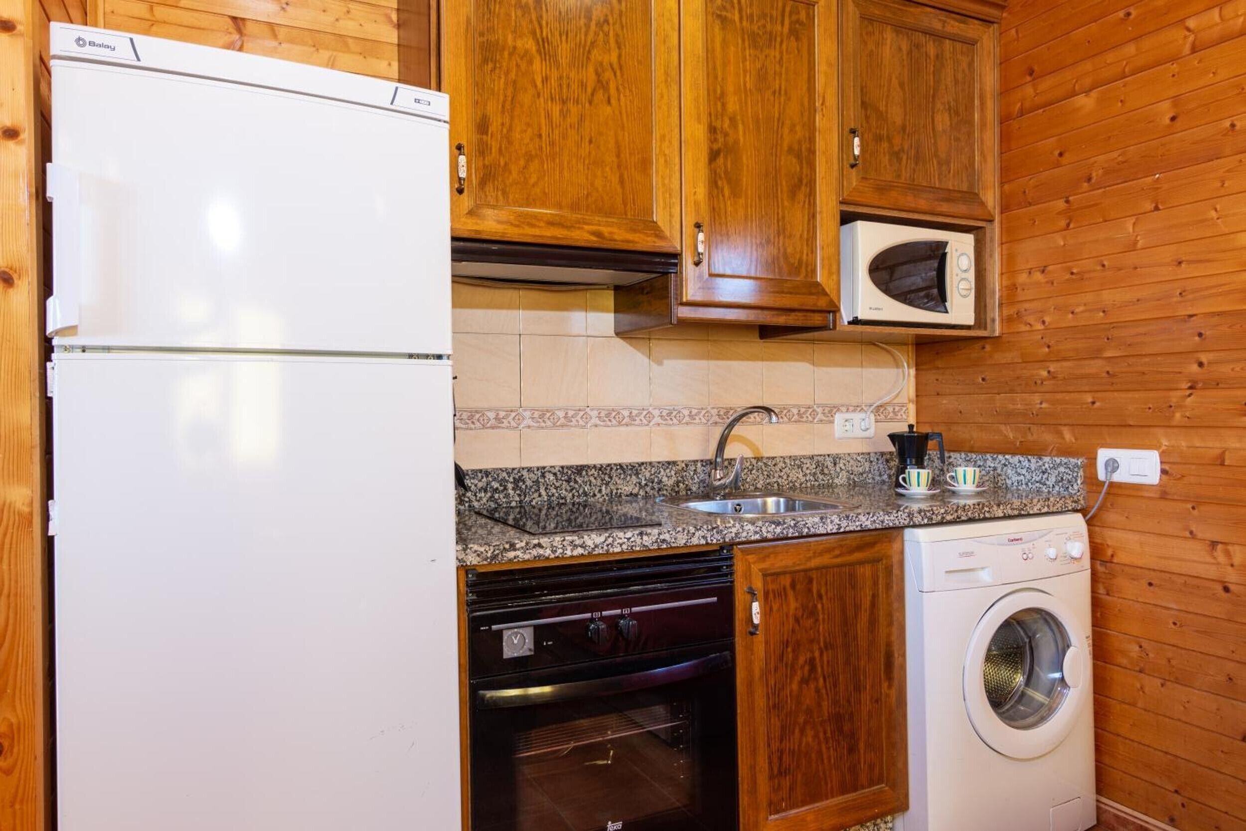 A compact kitchen with a refrigerator, microwave, oven, and washing machine.