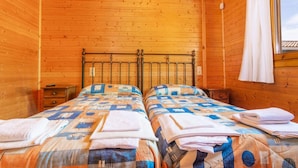 Een houten slaapkamer met twee bedden, een raam en een gordijn.
