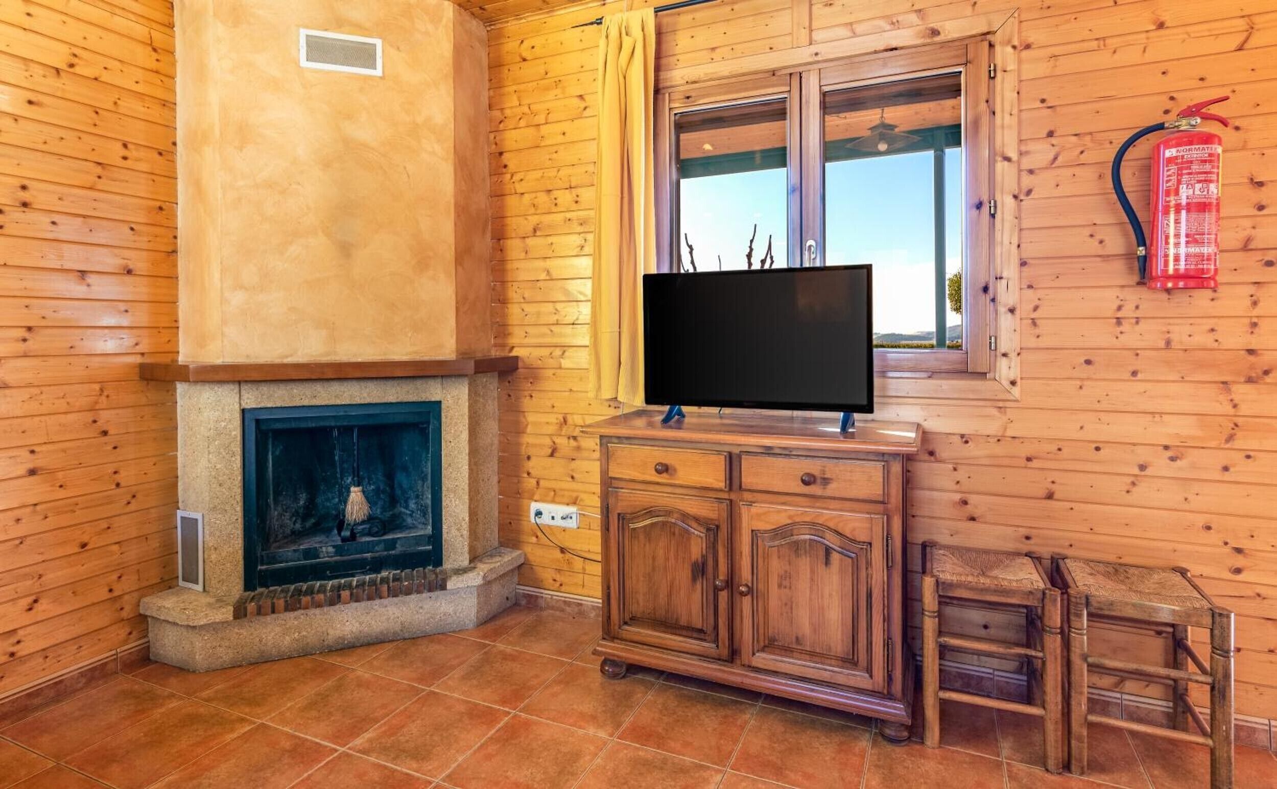 A room with wooden walls, a fireplace, a television on a wooden stand, and a fire extinguisher mounted on the wall.
