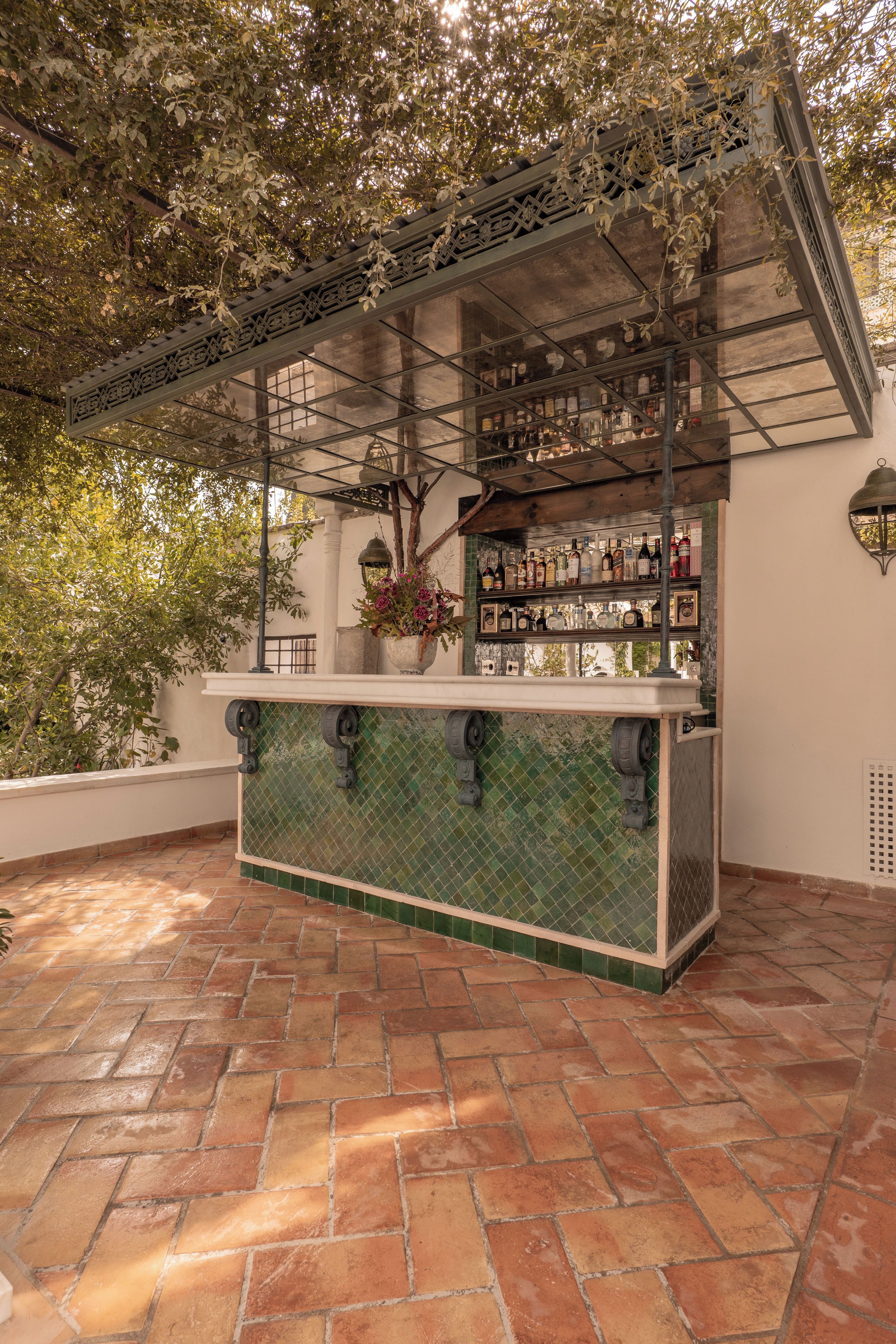 An outdoor bar area with a tiled floor, a glass enclosure, and a variety of bottles.