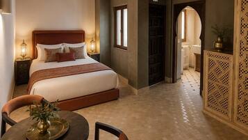 Habitación de hotel con una cama grande, techo de madera, mesa de comedor con sillas y un mueble decorativo.
