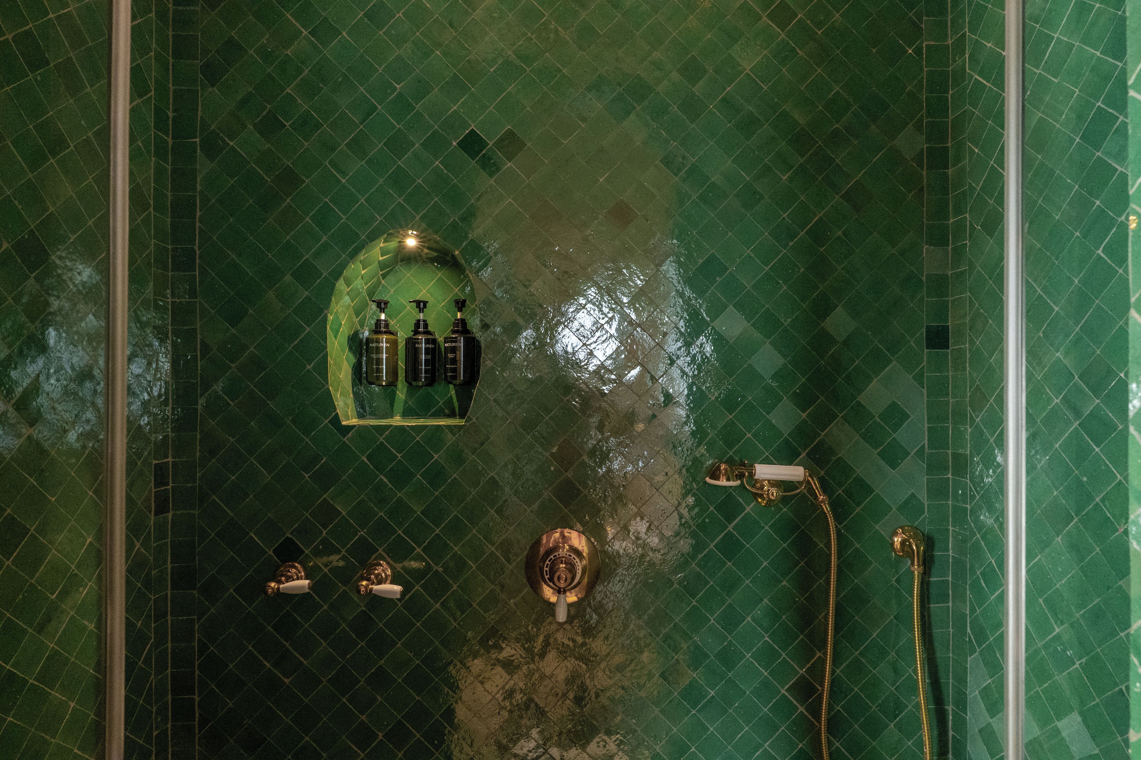 A bathroom with a green tiled floor, a shower area, and a sink with a faucet.