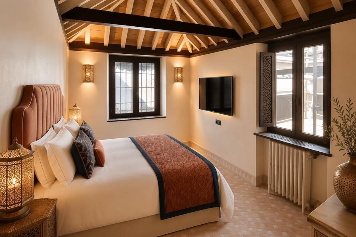 A bedroom with a large bed, a TV mounted on the wall, and a window with a view.