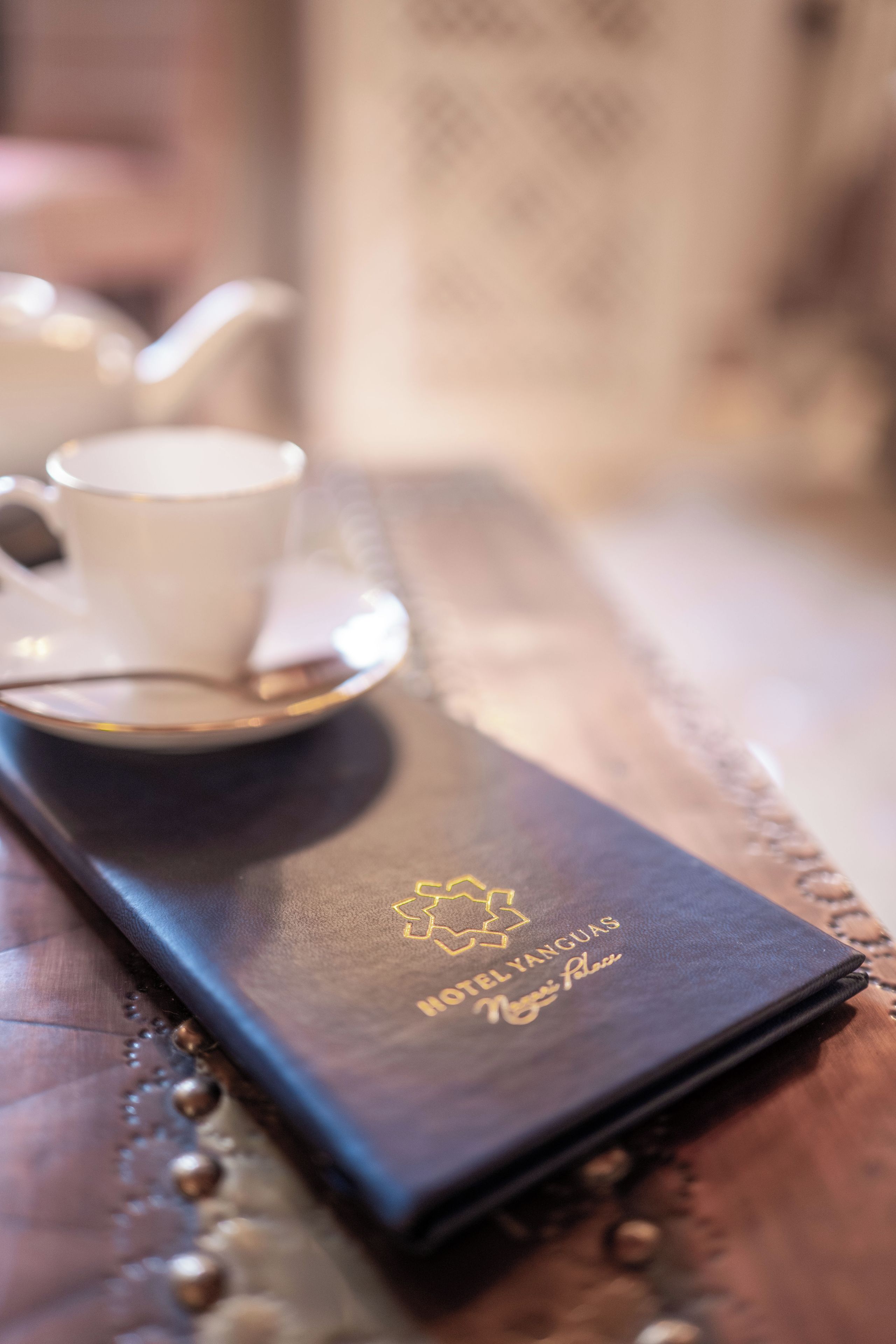 A leather-bound notebook with 'HOTEL YANGUAS' embossed on it, placed on a table with a cup and saucer.