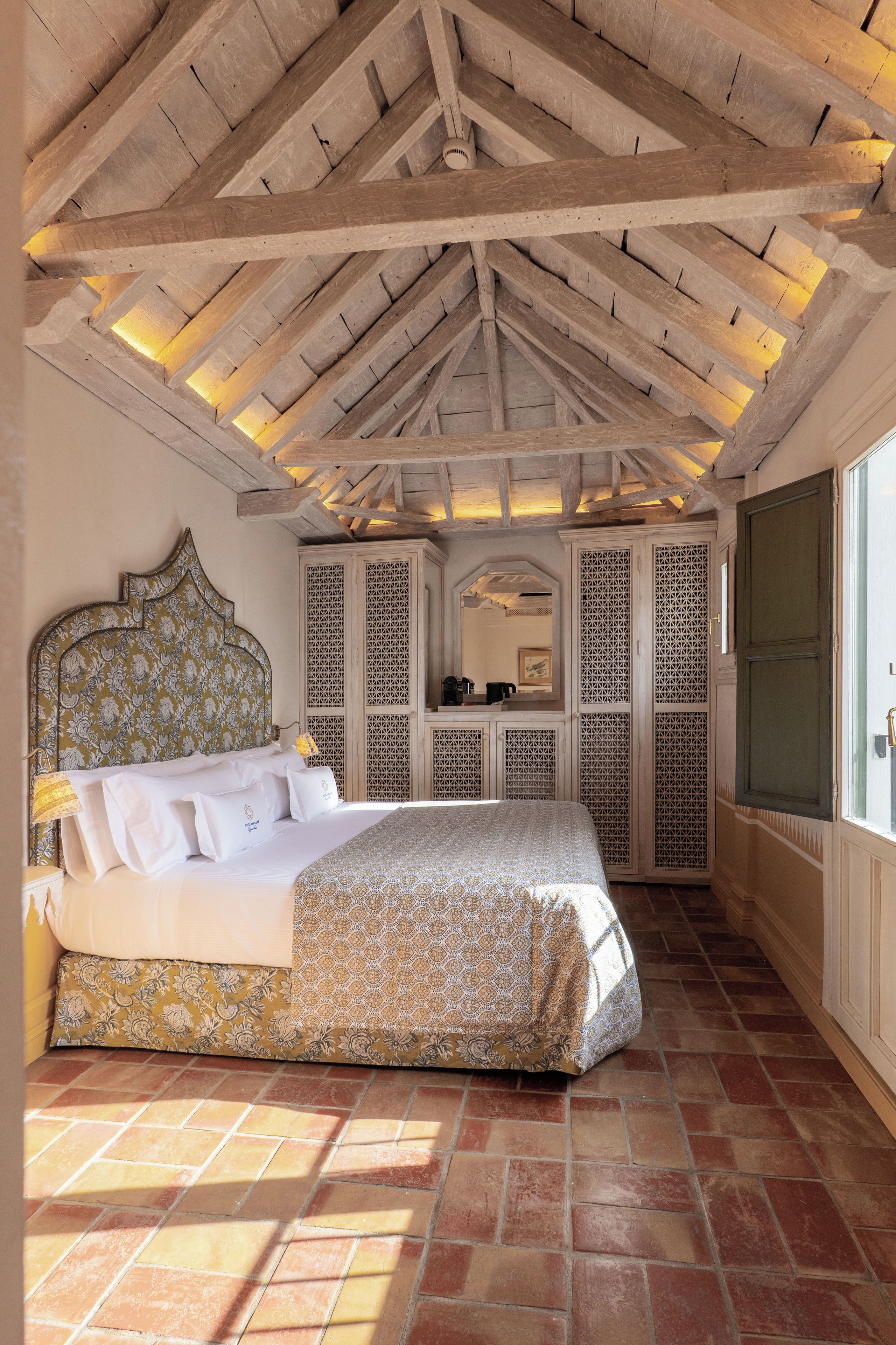 A bedroom with a large bed, a wooden ceiling, and a view of the outside.