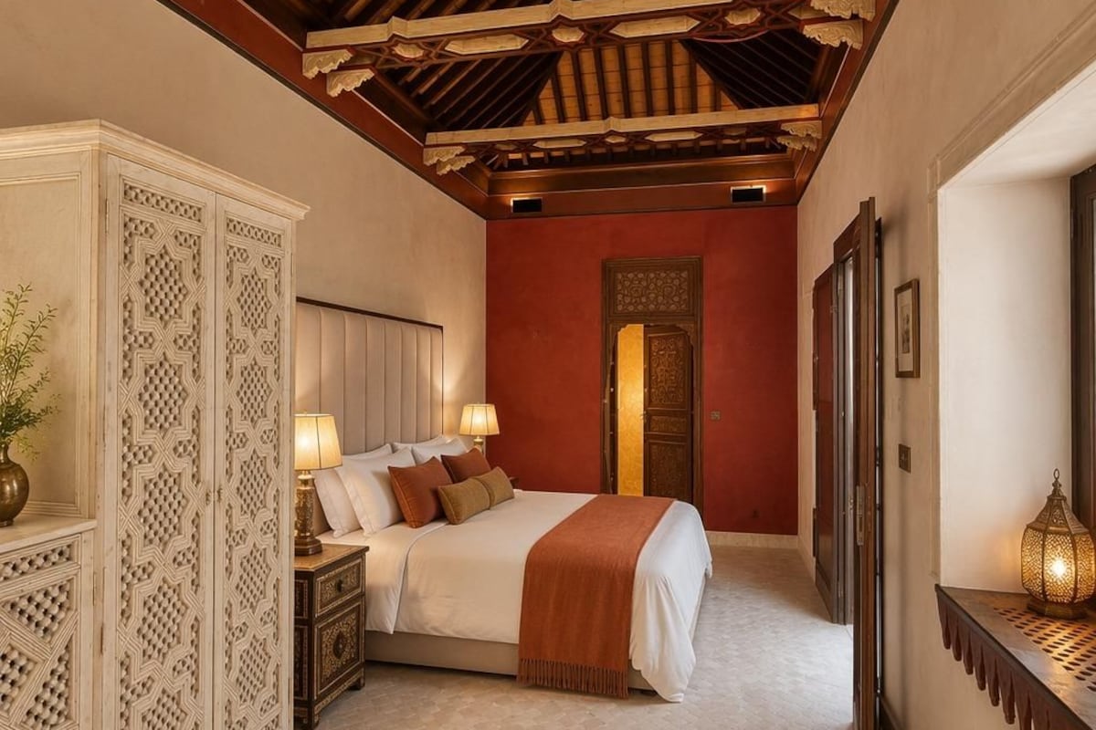 A bedroom with a bed, nightstands, a decorative cabinet, a mirror, and a wall-mounted light fixture.