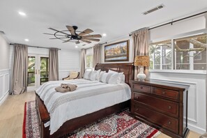 A bedroom with a bed, a nightstand, a dresser, a ceiling fan, and a window with curtains. - Folly Fun House – Just Steps to the Beach (Folly Beach)