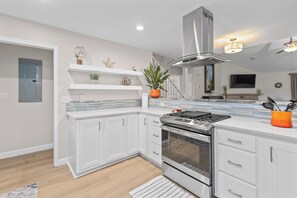 Une cuisine moderne avec des meubles blancs, un four encastré et une hotte de cuisson en acier inoxydable.