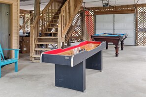 A pool table in a room with a wooden staircase and a garage door in the background. - Folly Fun House – Just Steps to the Beach (Folly Beach)