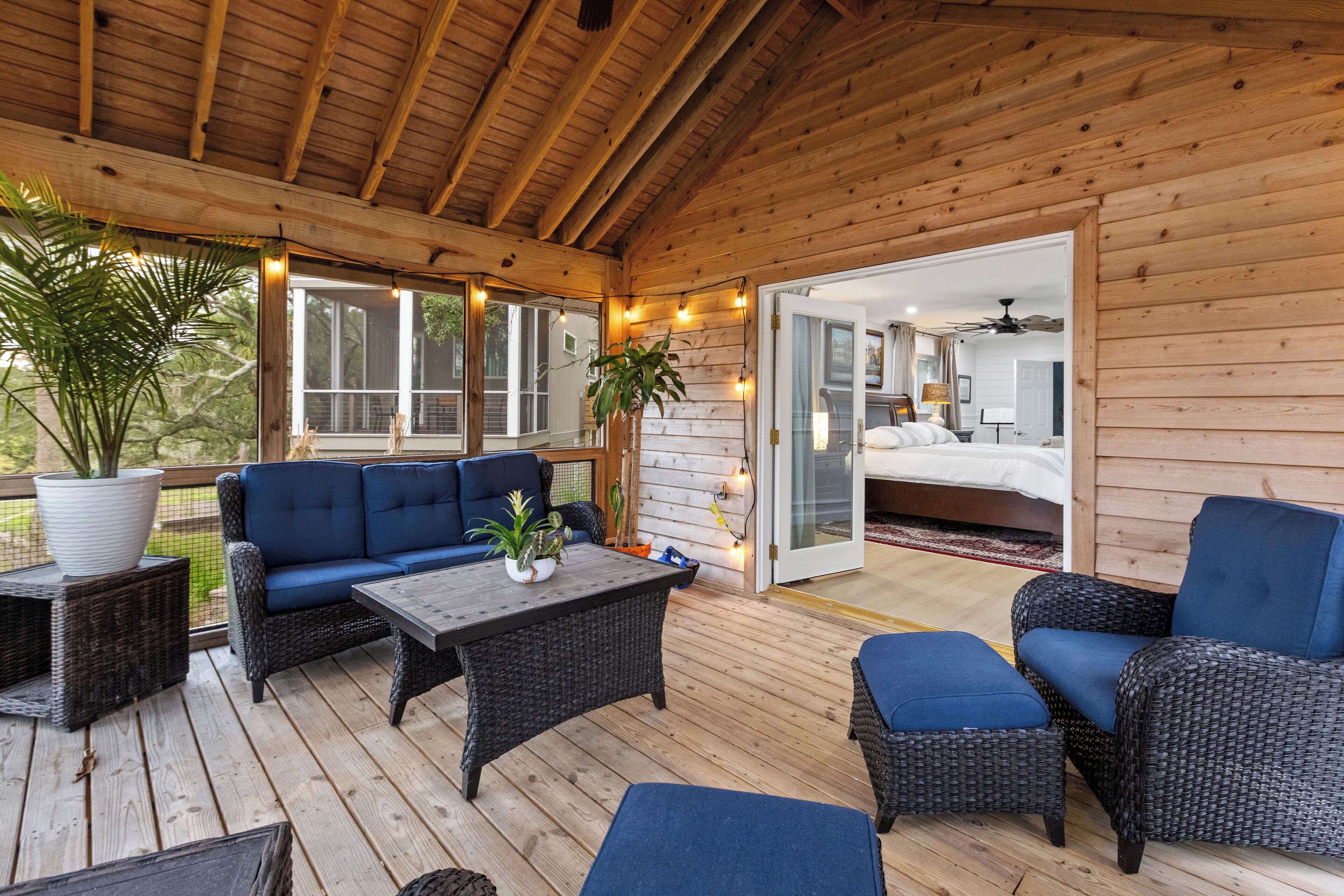 A wooden deck with outdoor furniture, a glass door leading to a bedroom, and string lights.
