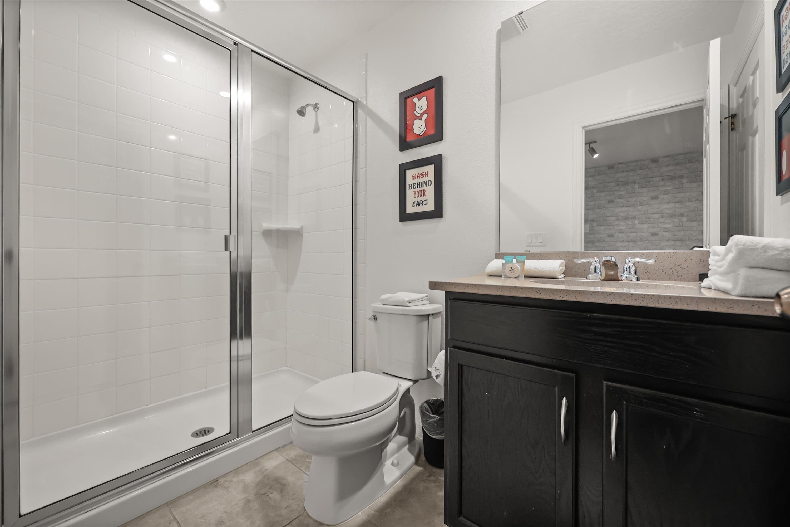 Un baño moderno con cabina de ducha de vidrio, inodoro y tocador con espejo.