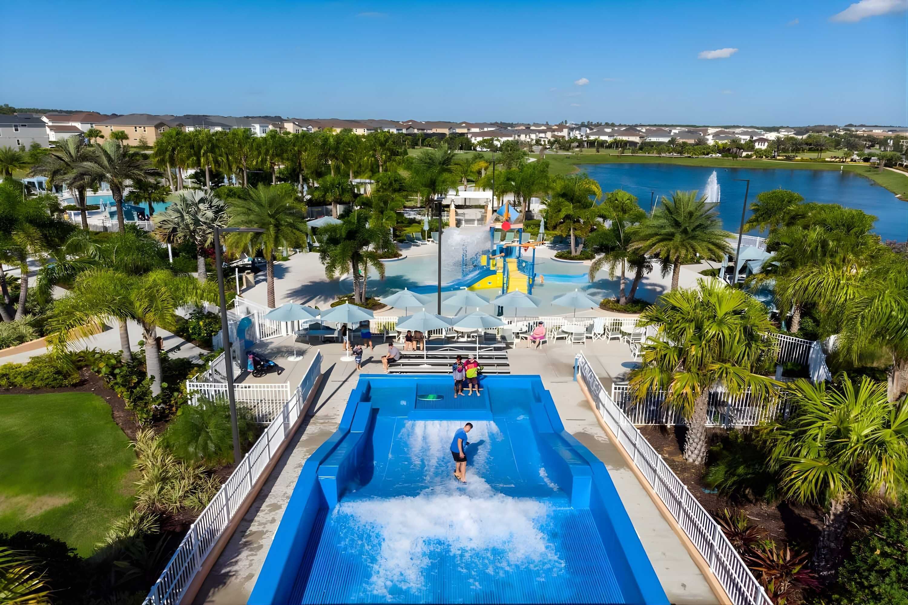 Parque aquático com uma piscina grande, palmeiras e vista para um lago.