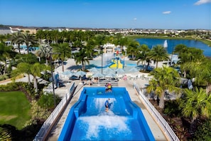 Parque aquático com uma piscina grande, palmeiras e vista para um lago.