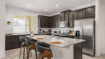 A modern kitchen with dark cabinets, stainless steel appliances, and a central island with bar stools.