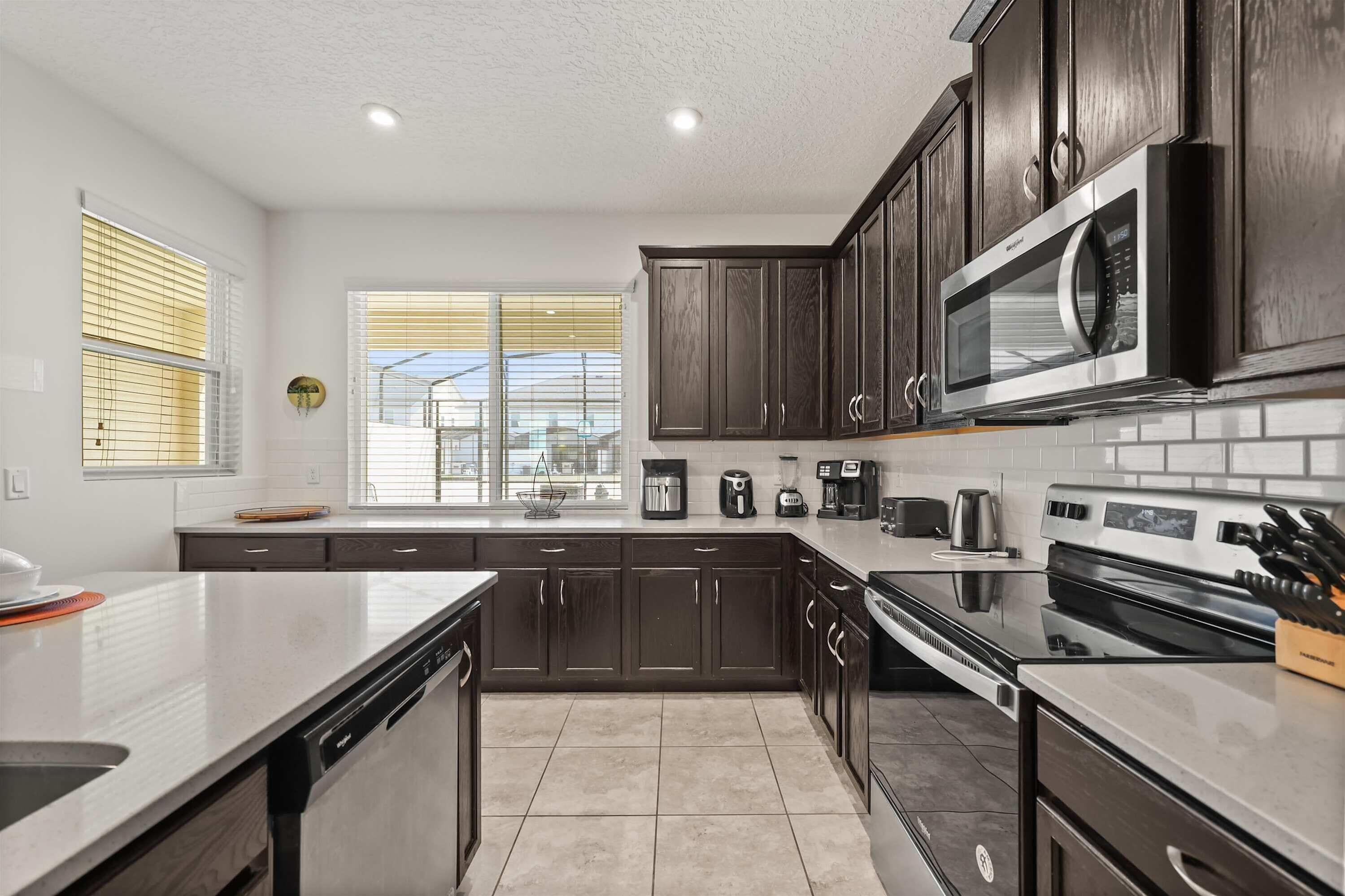 A modern kitchen with dark wooden cabinets, stainless steel appliances, and a large window with blinds.