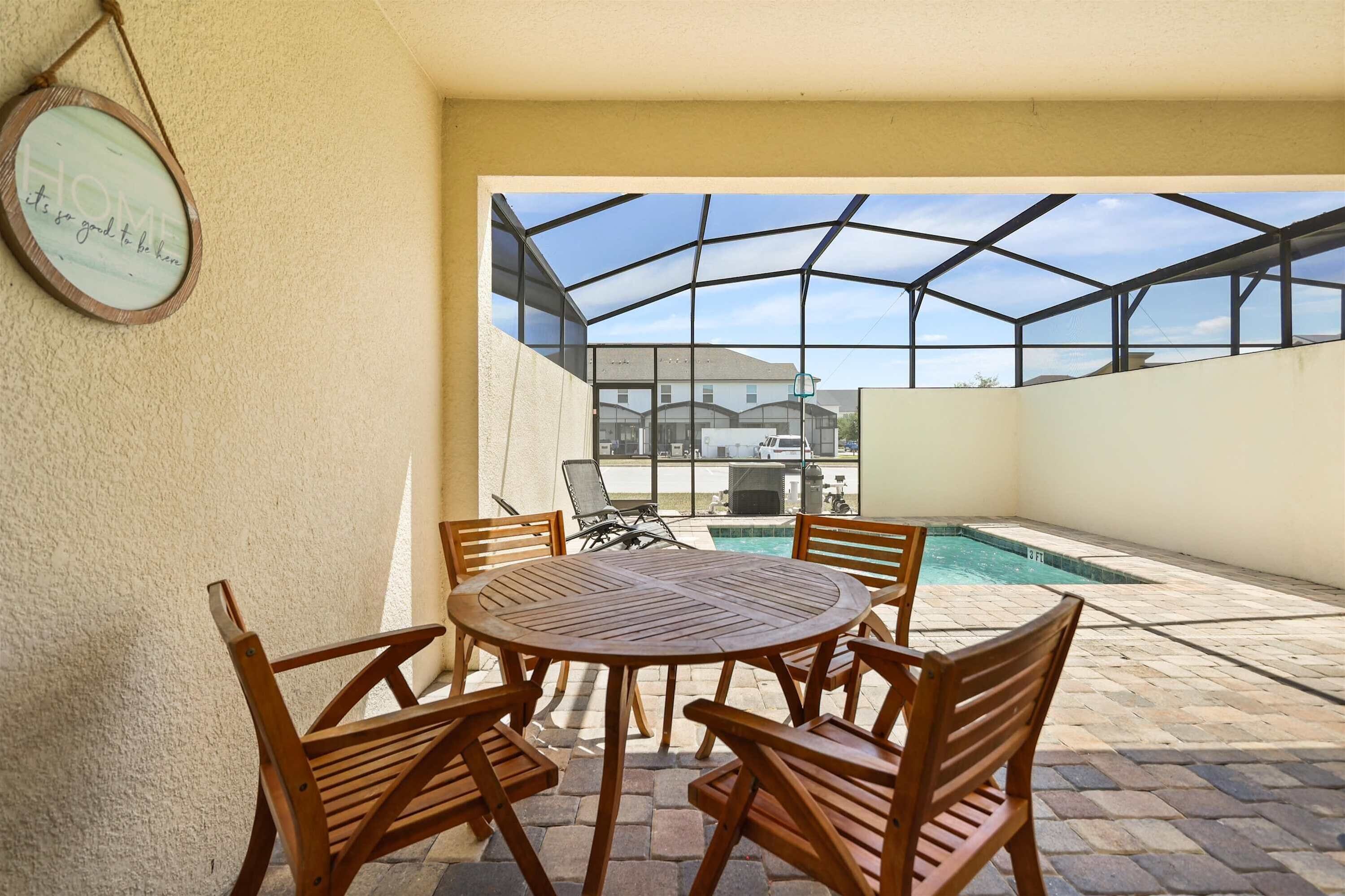 Un patio con una mesa y sillas de madera redonda, piscina y vista de edificios al fondo.