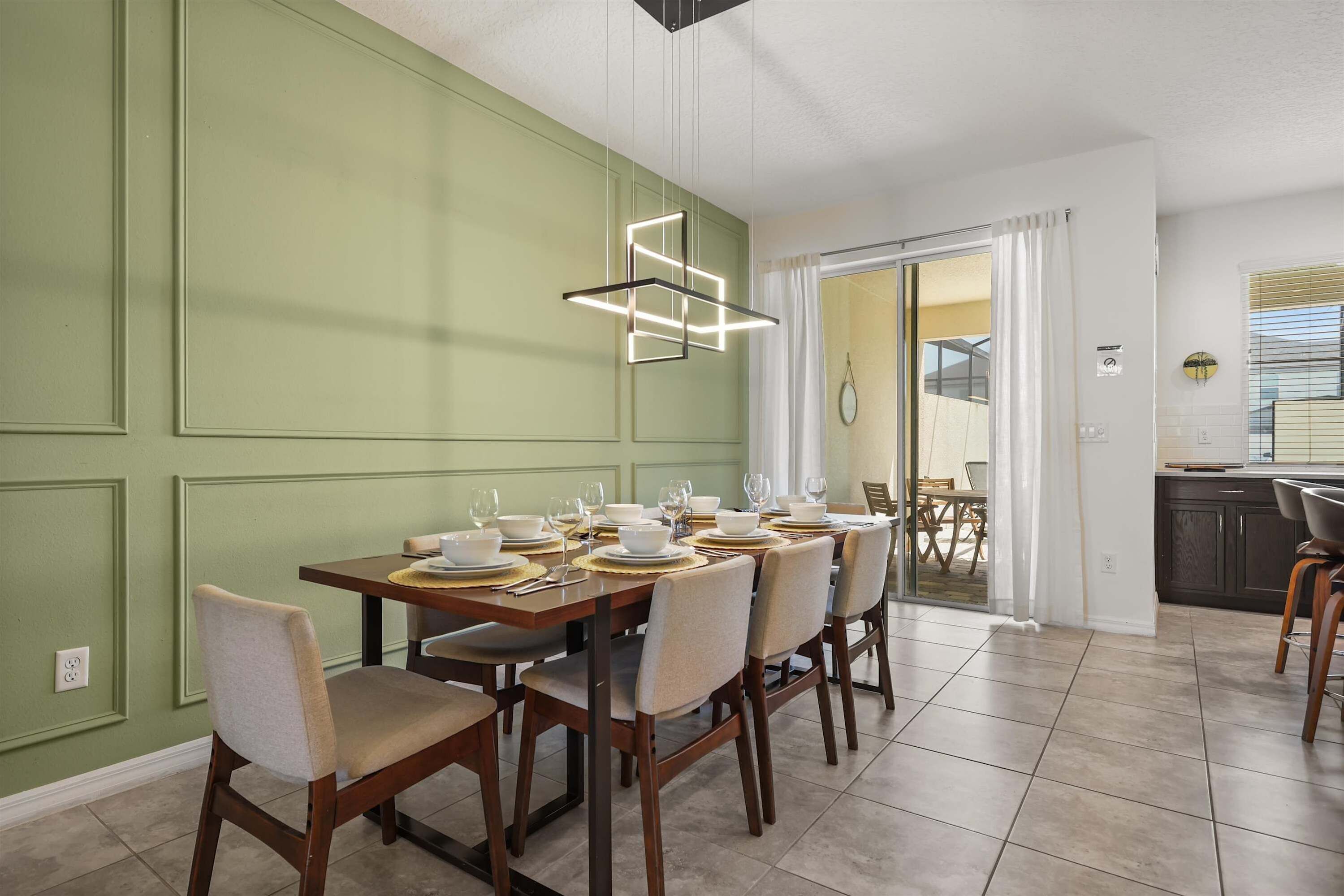 A dining area with a table set for six, chairs, a modern pendant light, and a view into the kitchen.