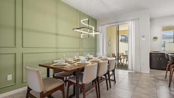 A dining area with a table set for six, chairs, a modern pendant light, and a view into the kitchen.