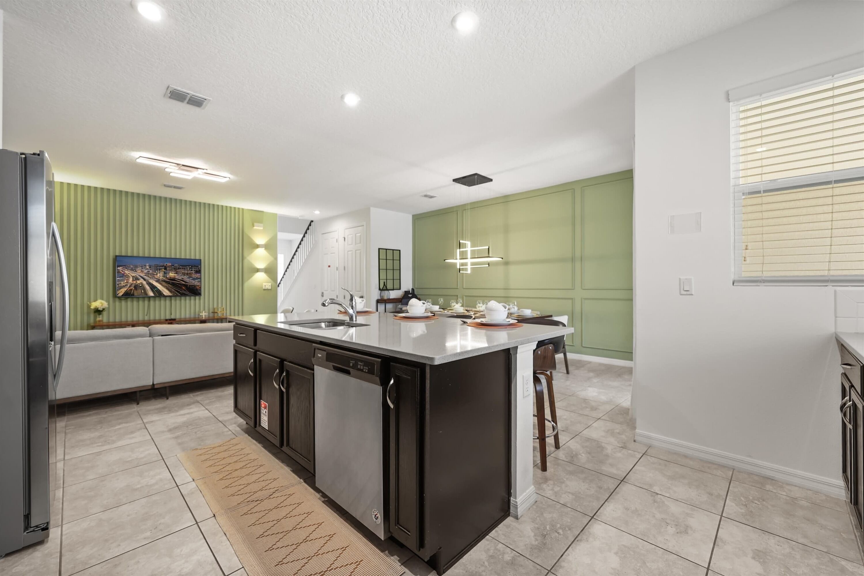 A modern kitchen with a central island, built-in appliances, and a green accent wall.