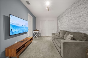 A living room with a flat-screen TV, a wooden TV stand, a grey sofa, a white coffee table, and a brick-patterned wall. - Upstay Modern Home Near Disney With Pool (Kissimmee)