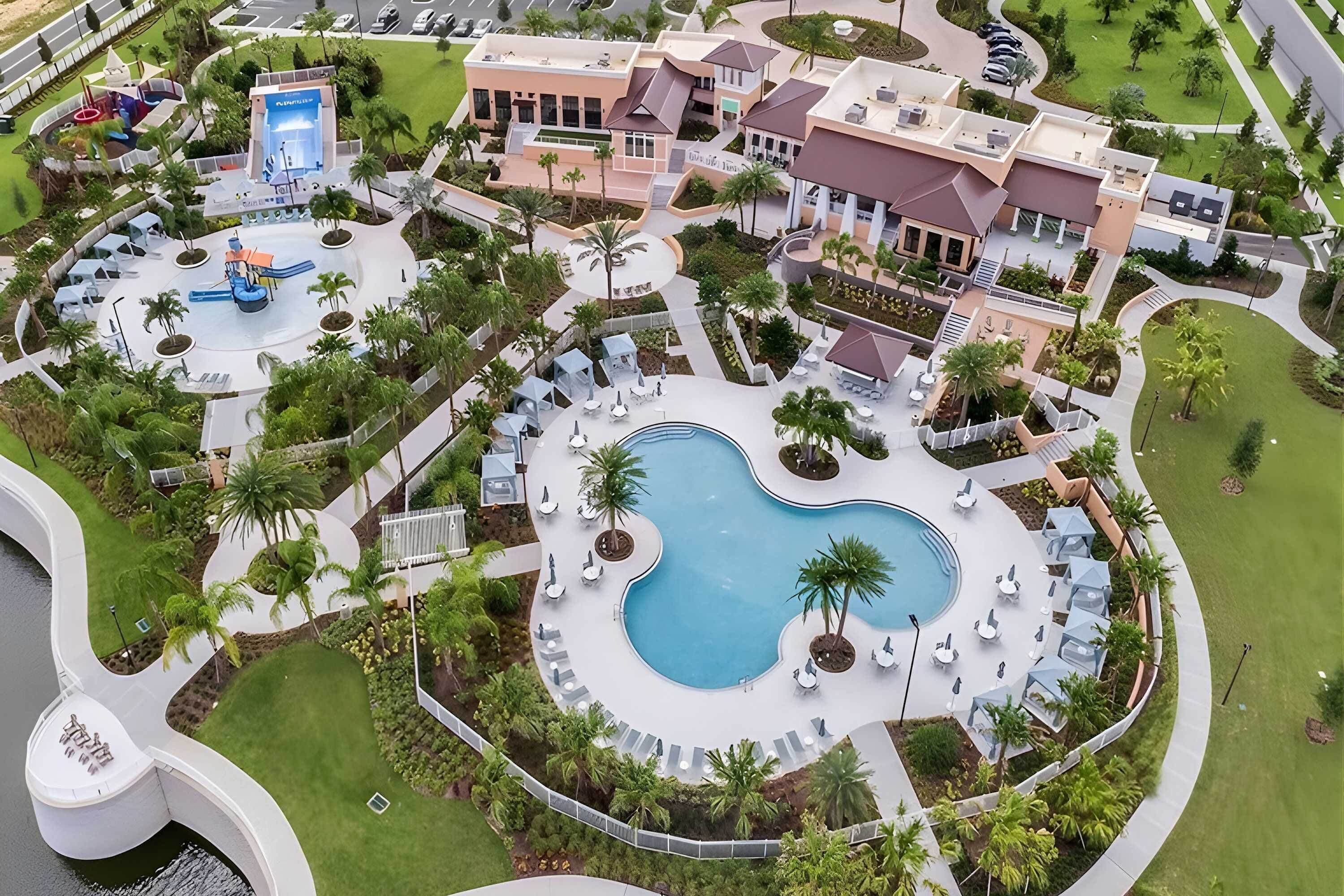 Eine Luftaufnahme eines Resorts mit einem zentralen Schwimmbecken, einer Wasserrutsche und verschiedenen Sitzbereichen im Freien, umgeben von Palmen.