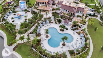 Eine Luftaufnahme eines Resorts mit einem zentralen Schwimmbecken, einer Wasserrutsche und verschiedenen Sitzbereichen im Freien, umgeben von Palmen.