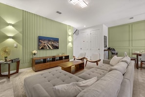 A living room with a sectional sofa, a coffee table, a TV on the wall, and a dining area with a table and chairs. - Upstay Modern Home Near Disney With Pool (Kissimmee)