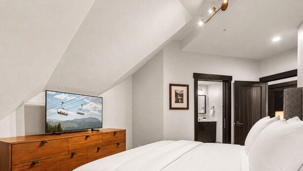 Une chambre à coucher avec un lit, une commode en bois et un téléviseur diffusant une vue sur la montagne.