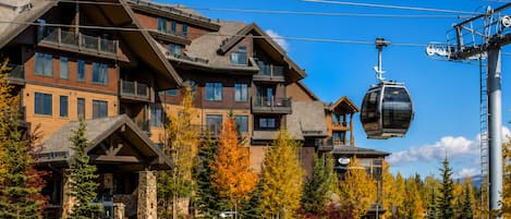 A multi-story building with a ski lift cable car in operation, surrounded by trees with autumn foliage.