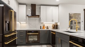 Une cuisine moderne avec des meubles de couleur sombre, des appareils en acier inoxydable et un plan de travail en marbre.